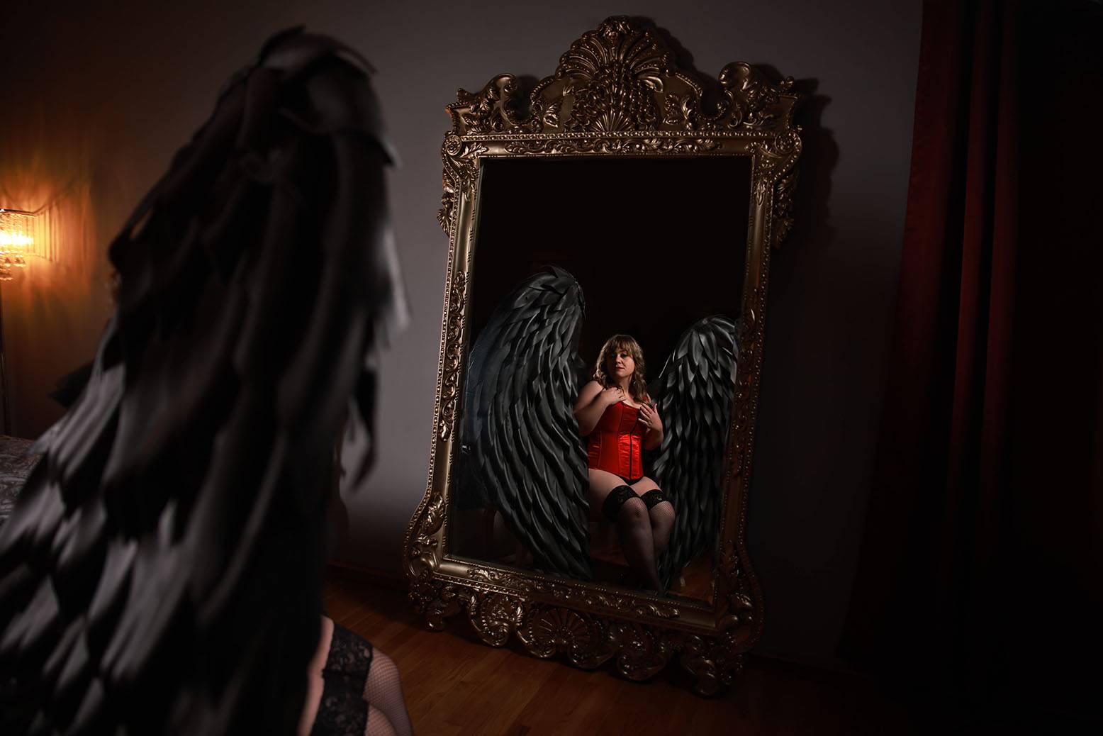 Boudoir portrait with dark lighting of woman posing in mirror wearing grey wings prop